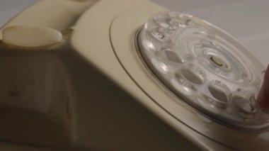 A mans hand removing the handset and rotating the dialer with his finger. Male finger dialing phone number on an old white rotary telephone with disc dial. Retro plastic phone. The concept of