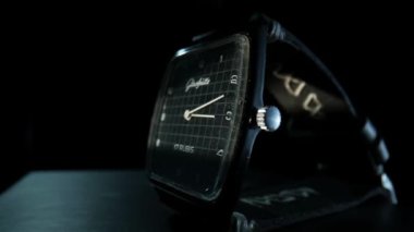 Old black wrist watch with handmade leather wristlet with running hour and minute hands in timelapse video. Ticking antique wrist watch isolated on black studio background. Movement of hands of a