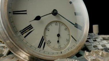 Silver vintage pocket watch dial on pile of clockwork parts. Round old clock among metal gears and cogwheels. Disassembled watch details and vintage pocket watch rotating on black studio background