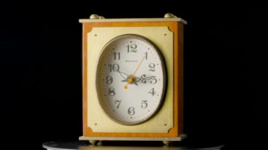 Old wooden clock with ticking hands. Brown vintage timepiece from USSR with wooden case rotating on an isolated black background. View of face and back. Table clock with numbers and spinning hands