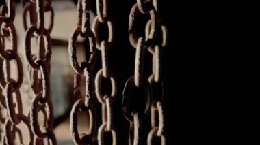 Rusty metal old chain dangling in dark indoor space. Close up of the links of an aged iron chain covered with corrosion and dust. Rough damaged metal structure. Grunge. Strong uneven metal connections