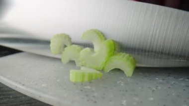 Male hands cutting celery stalks with a knife into small slices. Metal knife chopping celery on a gray plastic board on a restaurant kitchen table. Chef cooking vegan salad with raw healthy vegetables