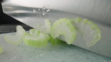 Male hands cutting celery stalks with a knife into small slices. Metal knife chopping celery on a gray plastic board on a restaurant kitchen table. Chef cooking vegan salad with raw healthy vegetables