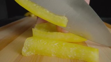 Hands of man with knife slicing yellow sweet pepper into long pieces. Process of cutting bell peppers in slices on wooden board. Preparation of salad from raw vegetables in the kitchen or restaurant