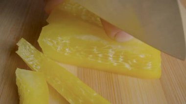 Hands of man with knife slicing yellow sweet pepper into long pieces. Process of cutting bell peppers in slices on wooden board. Preparation of salad from raw vegetables in the kitchen or restaurant