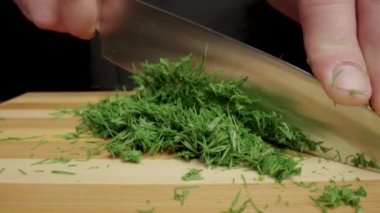 Male hands with a knife cutting green dill sprigs. Restaurant chef chopping greens on a wooden kitchen board. Preparing a salad with raw healthy vegetables and herbs. Vegetarian diet. Chopped fresh