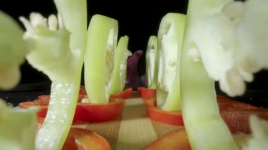 Camera movement along the rows of sweet peppers cut into rings. Red and yellow ripe raw bell peppers with pulp and seeds on a black isolated background. Sweet pepper slices on wooden board