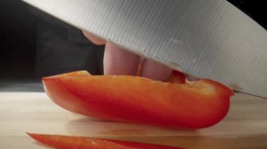 Hands of man with knife slicing red sweet pepper into long pieces. Process of cutting bell peppers in slices on wooden board. Preparation of salad from raw vegetables in the kitchen or restaurant