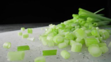Pieces of green onion stalks chopped on a gray plastic board. Slices of fresh green scallion on a black isolated background. Chopped shallots or chive, seasonal greenery, seasoning for salad. Macro