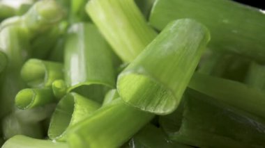 Green onion stalks cut into pieces on a wooden board. A heap of chopped green onions on a black isolated studio background. Seasonal greens, seasoning for fresh vegetable salad. Macro shot. Slow