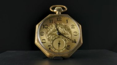 Gold vintage pocket watch with hands running in a circle in timelapse video. Old pocket watch with round dial and ticking hands. Vintage golden watch standing on table, isolated on black studio