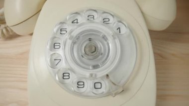 Old white rotary telephone with twisted cord on beige wooden table. Retro landline phone with rotary dialer and handset. Vintage analog plastic rotary telephone with dialing disk. Concept of