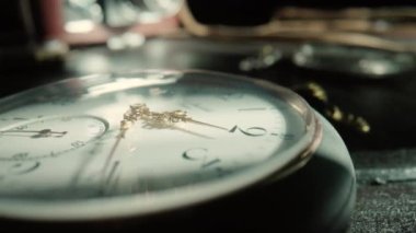 Silver antique pocket watch with ticking gold hands and vintage camera in background. An old round dial of a pocket watch lying on a dark wooden table. Running clock hands in circle. Time flow concept