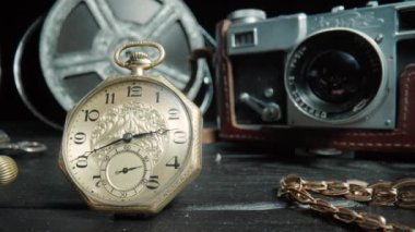 Antique gold and silver pocket watch, camera, gold chain and vintage film reel on black isolated background. Retro pocket watch with ticking second hand. Vintage objects are laid out on dark wooden