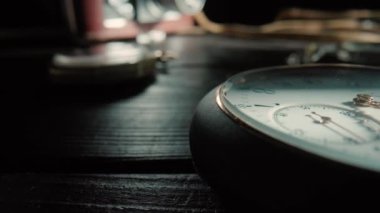 Silver antique pocket watch with ticking gold hands and vintage camera in background. An old round dial of a pocket watch lying on a dark wooden table. Running clock hands in circle. Time flow concept