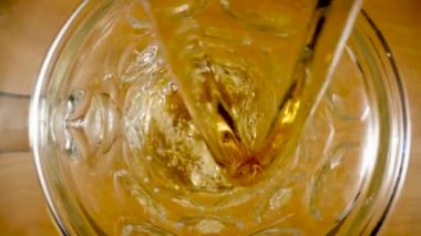 Top view of stream of amber beer pouring into glass. Macro shot of jet of golden drink spilling inside glass, filling it up and forming foam and bubbles. Soda, oil, lager or cider pouring in slow
