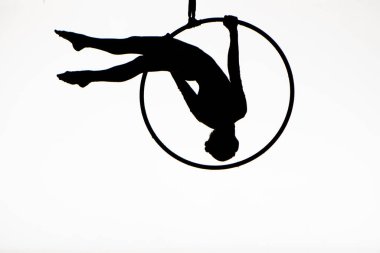 Black silhouette of a young woman gymnast performing on an aerial hoop on a white isolated studio background. Female aerial acrobat performs tricks while hovering upside down. Circus show. Full frame