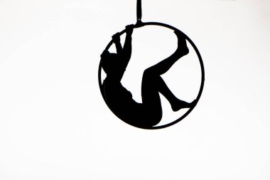 Black silhouette of a young woman posing on an air ring on an isolated white studio background. Female aerial acrobat performs tricks and balances on aerial hoop. Circus acrobatic show. Equilibrist