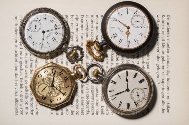 A set of antique gold and silver American and Swiss pocket watches with markings, lying on pages of an open book. Round old clock with white dials, hands and numbers. Presentation of vintage clocks