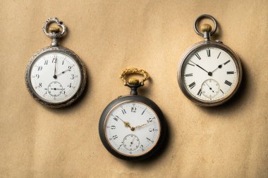 Set of three antique silver pocket watches with golden clockwork on beige background. Retro mechanical watch with white dials, hands and numbers. Presentation of old vintage round pocket watch for