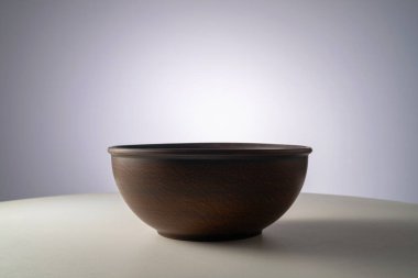 Empty earthen deep bowl on white table isolated on gray studio background. Brown handicraft ramekin or rustic plate. Empty earthenware, crockery from clay for food. Old dishes round shape