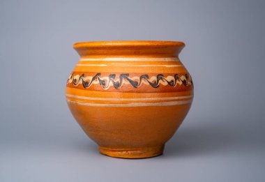 Yellow handmade pot made of clay with an ornament on a gray background in the studio. Earthenware for cooking. Kitchen utensils. Old brown rustic cookware made of earthen. Retro craft jug or ancient