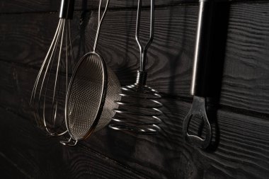 Opener, whisk, masher and strainer hanging against rustic grey wall in a restaurant or home kitchen. Kitchen utensils made of stainless steel or metal. Set of tools for cooking food. Kitchenware on