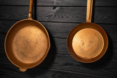 Two rustic copper fryingpans hanging on grey kitchen wall in restaurant or at home. Round empty gold or yellow pans with handles. Kitchenware, utensils for cooking and frying, interior decoration