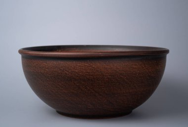 Empty earthen deep bowl on grey background. Brown handicraft ramekin. Empty earthenware, crockery from clay for food. Old dishes round shape
