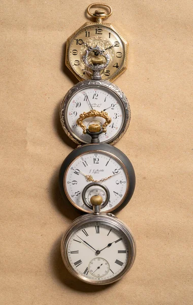 Vertical row of four antique American and Swiss pocket watches with markings on beige background. Retro gold and silver watch with white dials, hands and numbers. Presentation of old vintage round