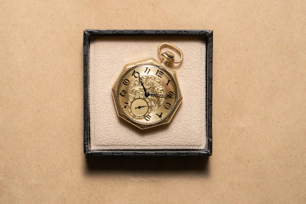 Golden vintage octagonal pocket watch in a gift box on a beige background. Old retro clock with dial, hands and numbers. An antique watch for a gentleman, an expensive accessory