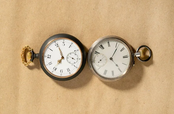 Two of antique silver pocket watches with golden clockwork on beige background. Retro mechanical watch with white dials, hands and numbers. Presentation of old vintage round pocket watch for gentlemen