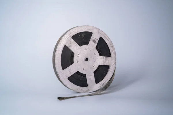 Old scratched metal reel with audio or video tape on a gray studio background. Bobbin, retro magnetic spool. Round reel for analogue projector or sound record. Videotape, filmstrip