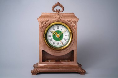 Old plastic table clock with gold stopped hands. Brown vintage watch with round white green dial and Roman numbers on isolated grey background. Front view of face aged clock. Retro timepiece, home