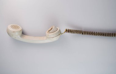 Dirty white remote telephone receiver from an old rotary landline phone with twisted cord on gray background. Plastic vintage handset with telephone cable. Retro home conversation apparatus. Photo in