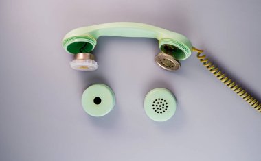 An old broken green telephone receiver with twisted cord on a gray background. Vintage untwisted telephone receiver. Disassembled handset from a retro landline phone. Top view
