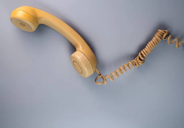 Yellow telephone receiver with twisted cord from an old antique rotary phone on blue background. Plastic removed handset from retro phone with cable. Concept of communication, conversation, connection