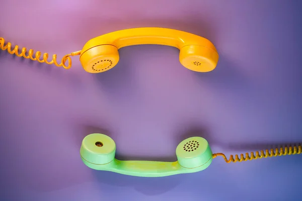 Yellow and green telephone receivers with twisted cords from an old antique rotary phones on purple background. Plastic removed handsets from retro phone with cable. Concept of communication