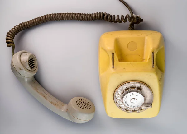Old yellow antique rotary telephone with grey removed receiver on blue background. Vintage landline home phone with dial, twisted cable and reciever handset. Communication, telecommunication