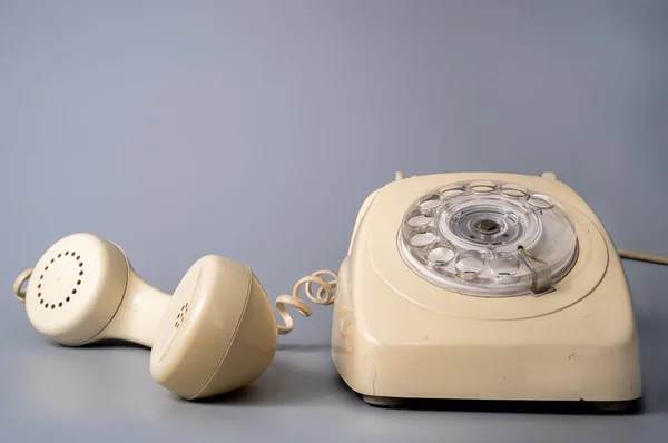 Old white rotary telephone with twisted cord on gray background. Retro landline phone with rotary dialer and remote handset. Vintage plastic rotary telephone with dialing disk. Concept of