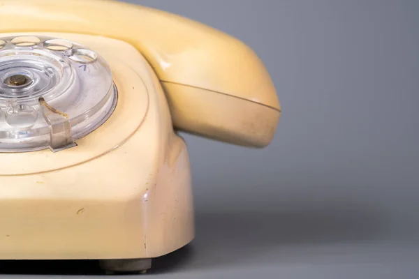 Old plastic landline telephone on a gray background. Retro yellow phone with handset, rotary dialer and holes with numbers. Vintage rotary telephone close up