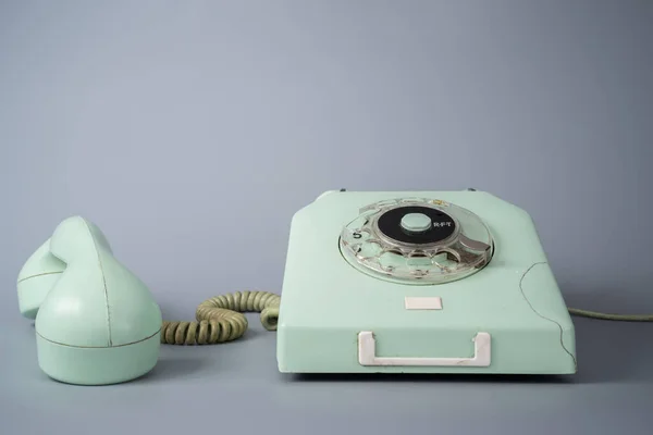 Old blue rotary telephone with twisted cord on gray background. Retro landline phone with rotary dialer and remote handset. Vintage plastic rotary telephone with dialing disk. Concept of communication
