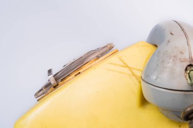 Side view of old plastic landline telephone on a gray background. Retro yellow phone with gray handset and rotary dialer. Vintage dirty, shabby rotary telephone close up