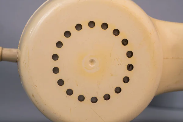 Tube from an old rotary landline phone. Macro shot of a yellow plastic telephone receiver with round holes. Removed phone handset with twisted cord on gray studio background. Vintage shabby phone