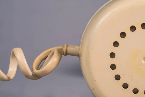 Tube from an old rotary landline phone. Macro shot of a yellow plastic telephone receiver with round holes. Removed phone handset with twisted cord on gray studio background. Vintage shabby phone