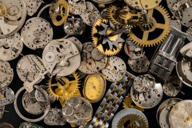 Top view of heap of metal internal parts of an old clock. Dial, clockwork, bracelet, gears, cogwheels on black studio background. Disassembled clock mechanism of an old clock. Clock parts in workshop