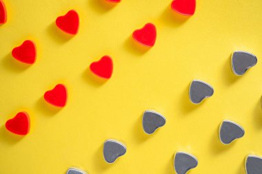 Pattern of rows of red and gray hearts on an isolated yellow studio background. Crystals, glisten confetti, spangles in form of hearts with reflective shadow. Symbol of love. Wallpaper for Valentines