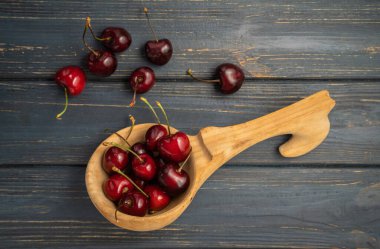 Red ripe sweet cherries lying in a wooden spoon on a dark gray wooden surface. Juicy summer berries in a wooden dipper on a rustic background. Background of organic fruits, wholesome food. Top view