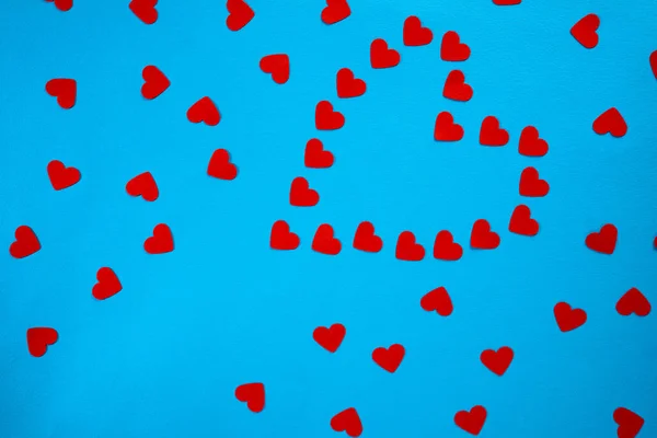 Pattern from red paper hearts laid out in the shape of a heart on a blue screen background. Holiday splash screen mockup for valentines day celebration. Red heart confetti, symbol of love, proposal
