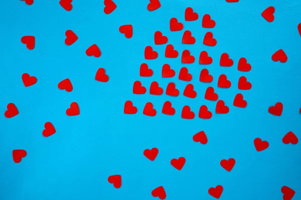 Pattern from red paper hearts laid out in the shape of a heart on a blue screen background. Holiday splash screen mockup for valentines day celebration. Red heart confetti, symbol of love, proposal